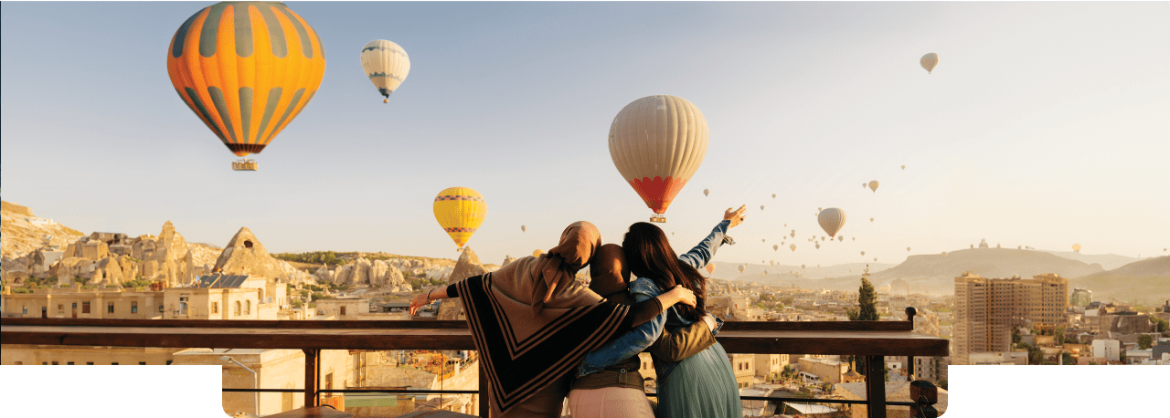 3 friends wrapping arms around each other while watching hot air balloons